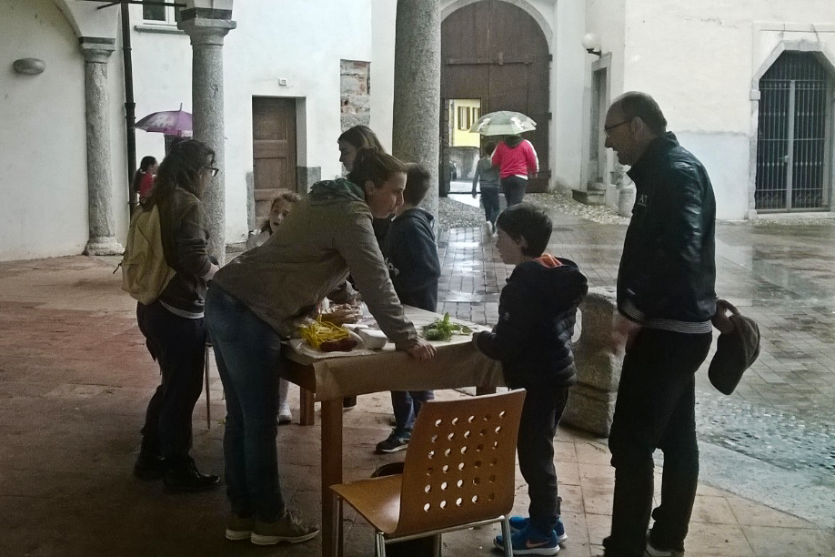 Adulti e bambini attorno a un banchetto all'interno dell'Orto Botanico di Valmadrera